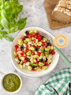 Sałatka z drobno posiekanymi pomidorkami, mozzarellą, oliwkami, pesto, ogórkiem i dodatkami.