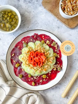 Pokrojony w cienkie plastry burak, na nim plastry ogórka, orzechy, kapary i łosoś, obłędnie doprawione.