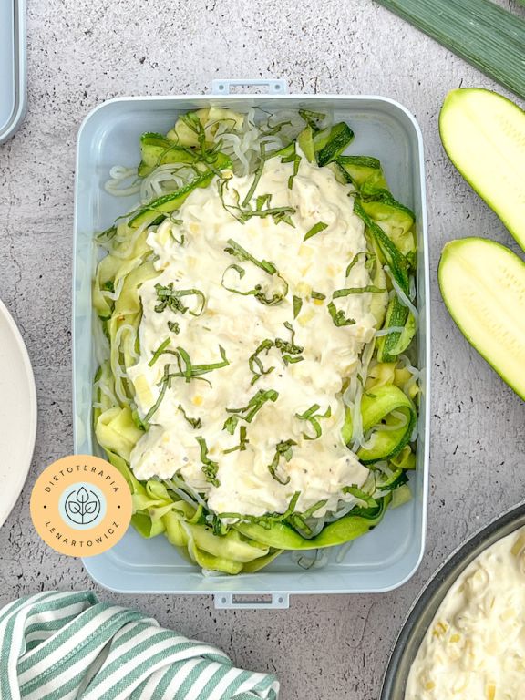 Danie obiadowe z makaronem i cukinią tagliatelle polanym białym sosem z kurczakiem, zapakowane w pudełku na wynos.