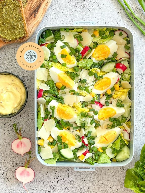 Sałatka cezar z jajkiem, rzodkiewką, kukurydzą, ogórkiem, aioli i dodatkami, zapakowana do pudełka na wynos.